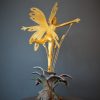 Bronze sculpture of a fairy covered in gold leaf with butterfly wings on top of a flower - back side