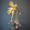 Bronze sculpture of a fairy covered in gold leaf with butterfly wings on top of a flower - left side