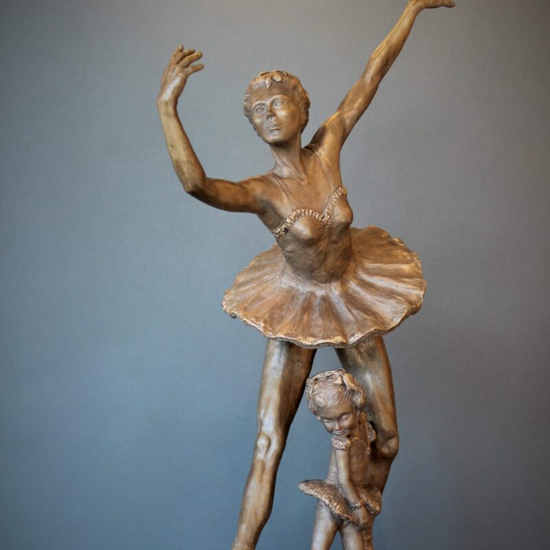 Bronze sculpture of daughter in tutu posing under mother ballerina