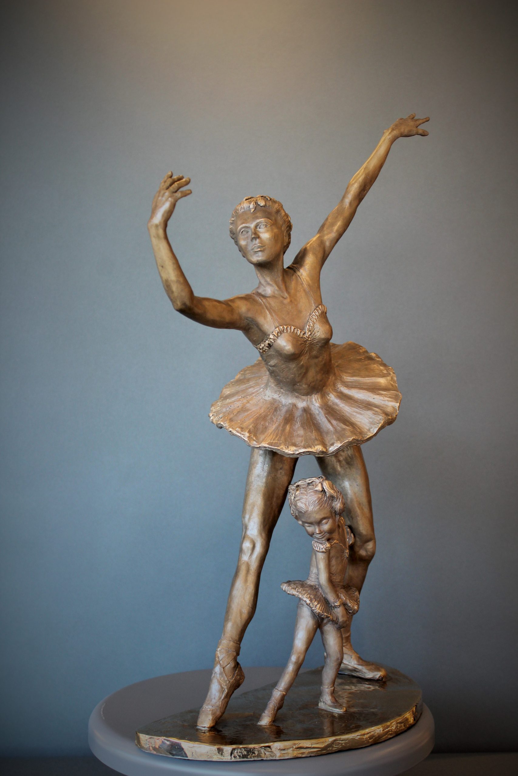 Bronze sculpture of daughter in tutu posing under mother ballerina