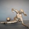 Bronze sculpture of a woman soccer player slide tackling the ball - left side view
