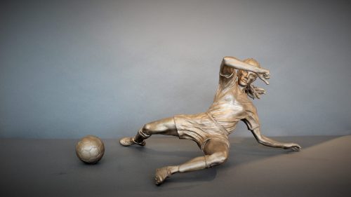 Bronze sculpture of a woman soccer player slide tackling the ball - front view