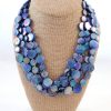 The Mother of Pearl Necklaces feature multiple strands of iridescent blue and purple shell discs, beautifully displayed on a beige fabric-covered bust.