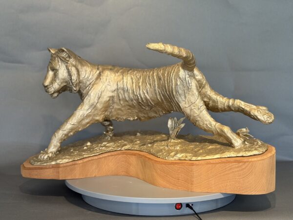 Naranji features a golden tiger sculpture in mid-stride on a wooden base with a gray circular platform, displayed against a plain gray background.