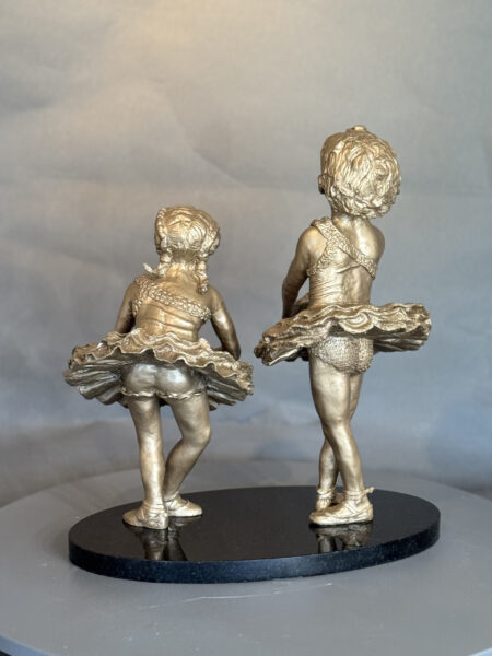 Showtime I and II are bronze sculptures of young ballerinas in tutus on a round black base, posed mid-dance with short hair, arms slightly bent, and detailed, textured costumes. Both figures face away from the viewer.