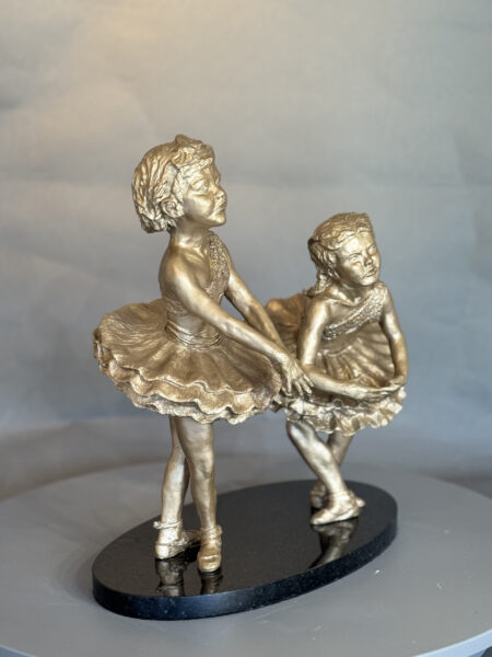 Showtime I and II is a bronze sculpture of two young ballerinas in tutus holding hands, standing on a black oval base, posed as if dancing together with detailed expressions and costumes.